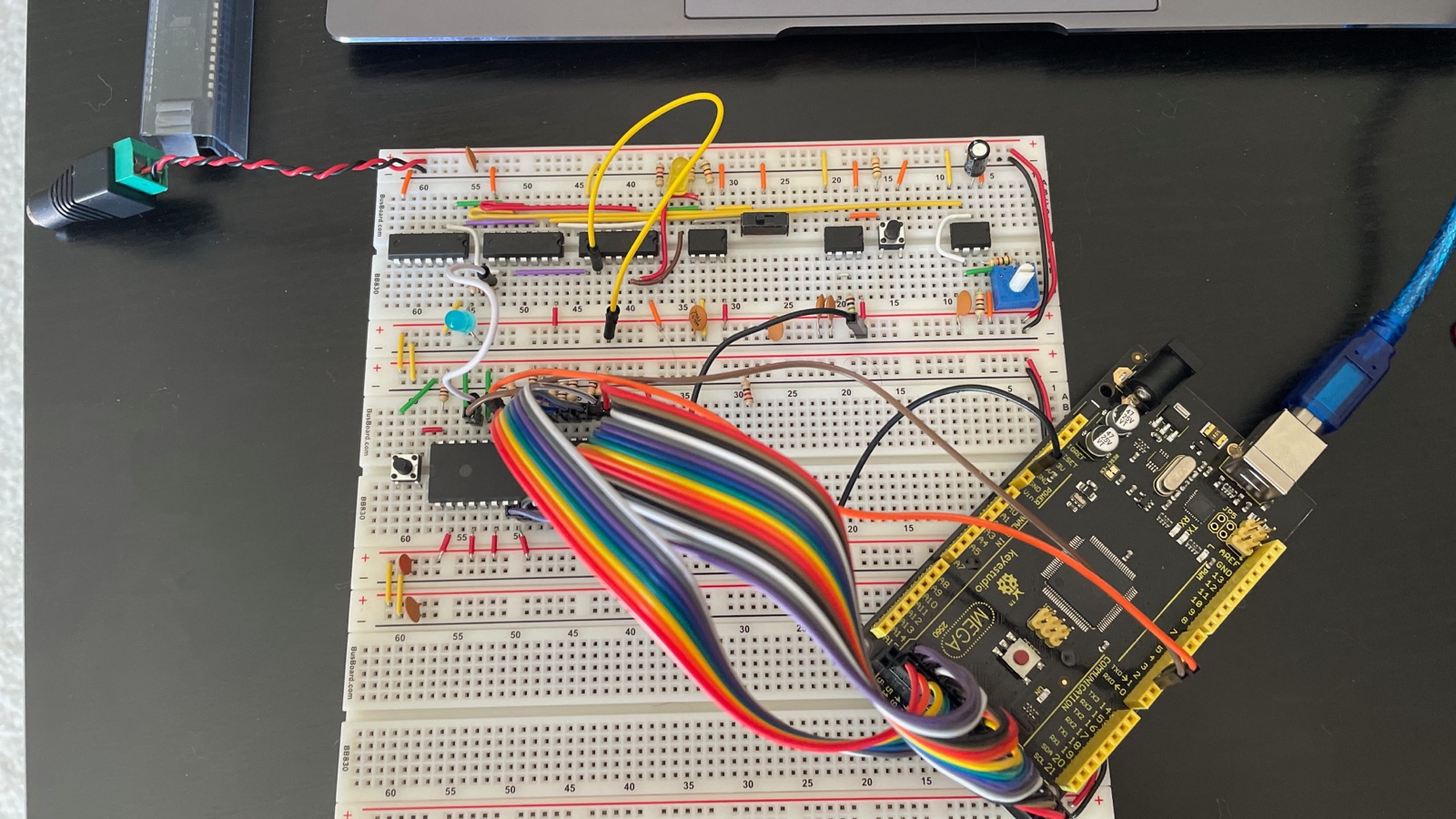 An Arduino Mega 2560 connected by rainbow ribbon cable to a bare 6502 on a breadboard, with a 555-based clock module on the board above it.