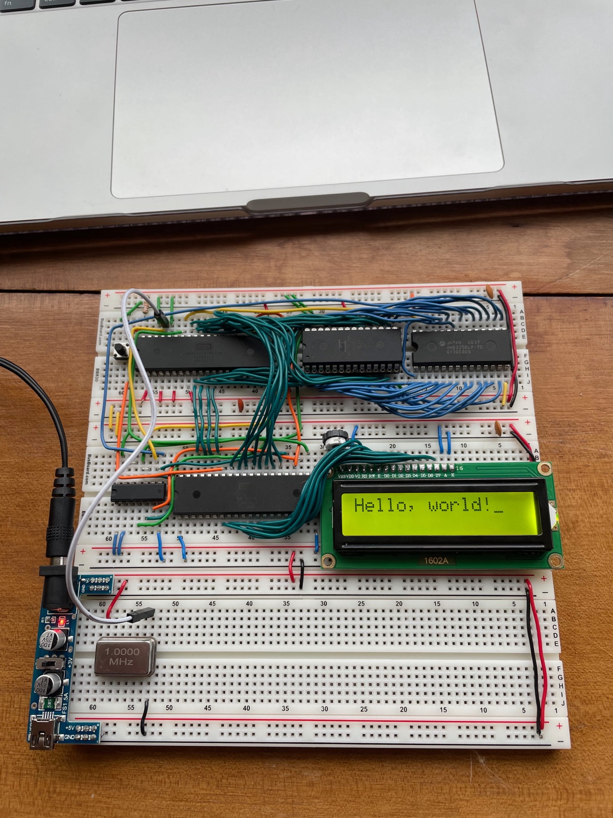 The finished 6502 breadboard computer displaying Hello, world! on a 1602 character LCD, with a 1 MHz oscillator can and a breadboard power supply module.